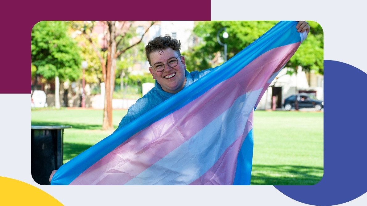 image of a smiling person holding up a trans flag